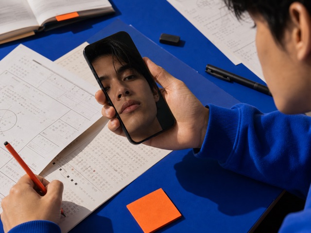 Student reflected in a phone above practice sheets